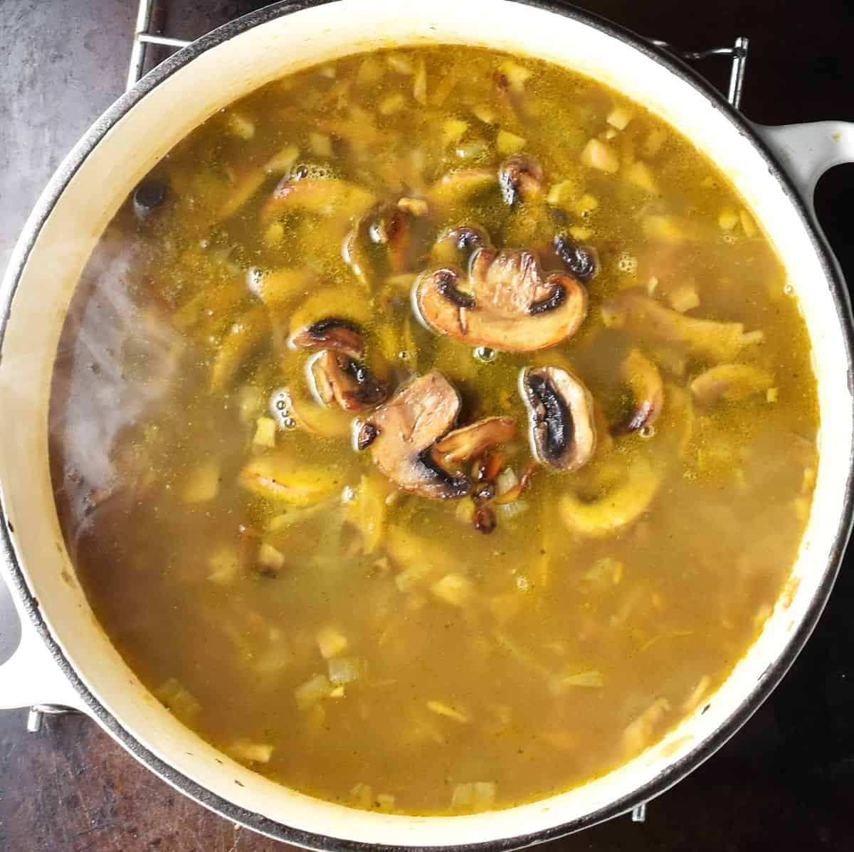 Close-up view of Polish mushroom soup with sliced mushrooms visible in white pot.