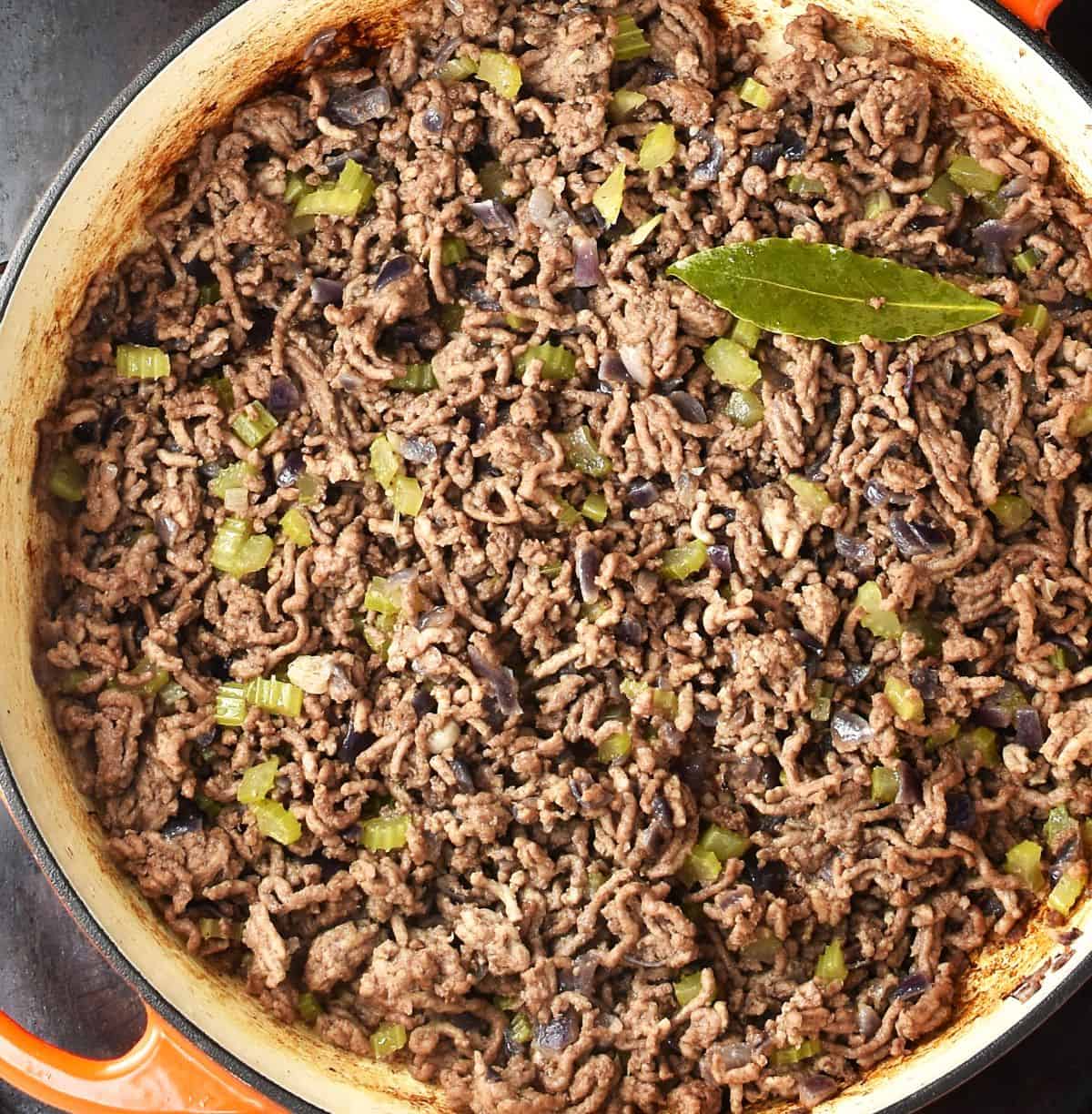 Top down view of ground meat with vegetables in large shallow pan.
