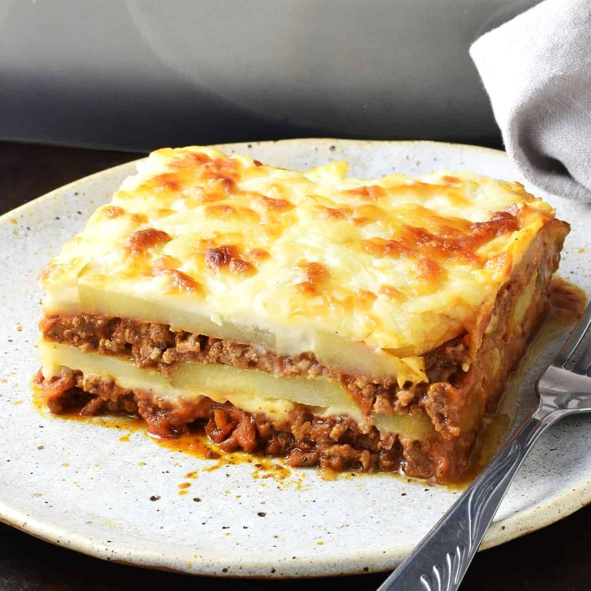 Side view of potato lasagna slice on plate with fork.