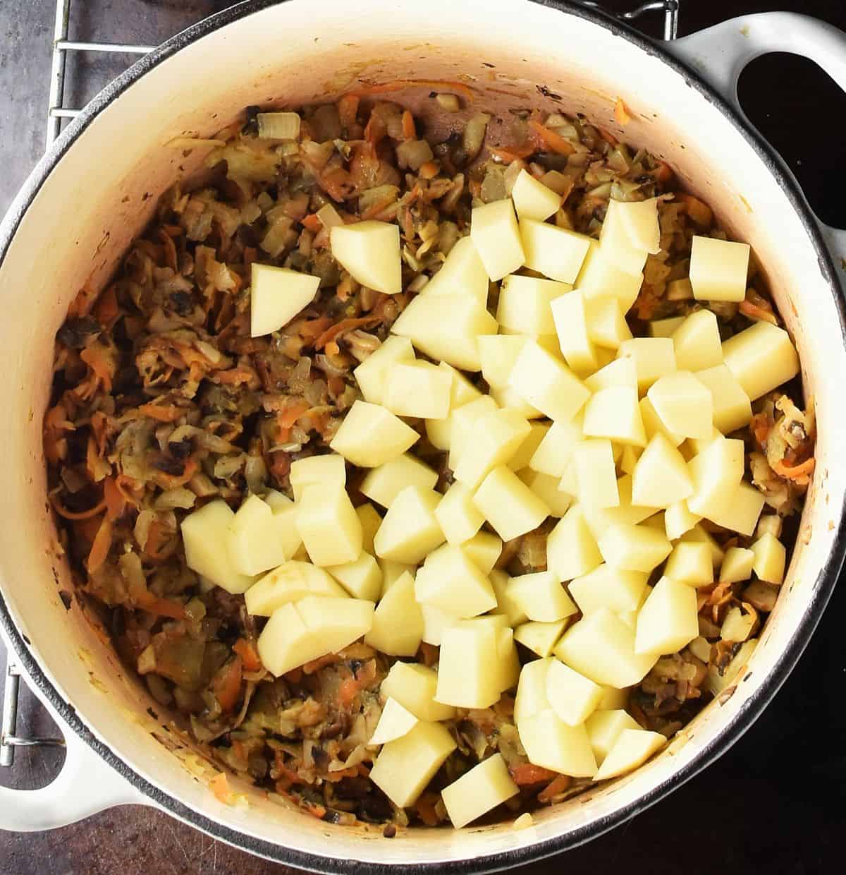 Cubed potatoes with Polish mushroom soup vegetable base in white pot.