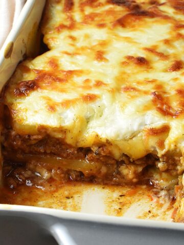 Side view of potato lasagna with meat filling and white sauce in rectangular dish.