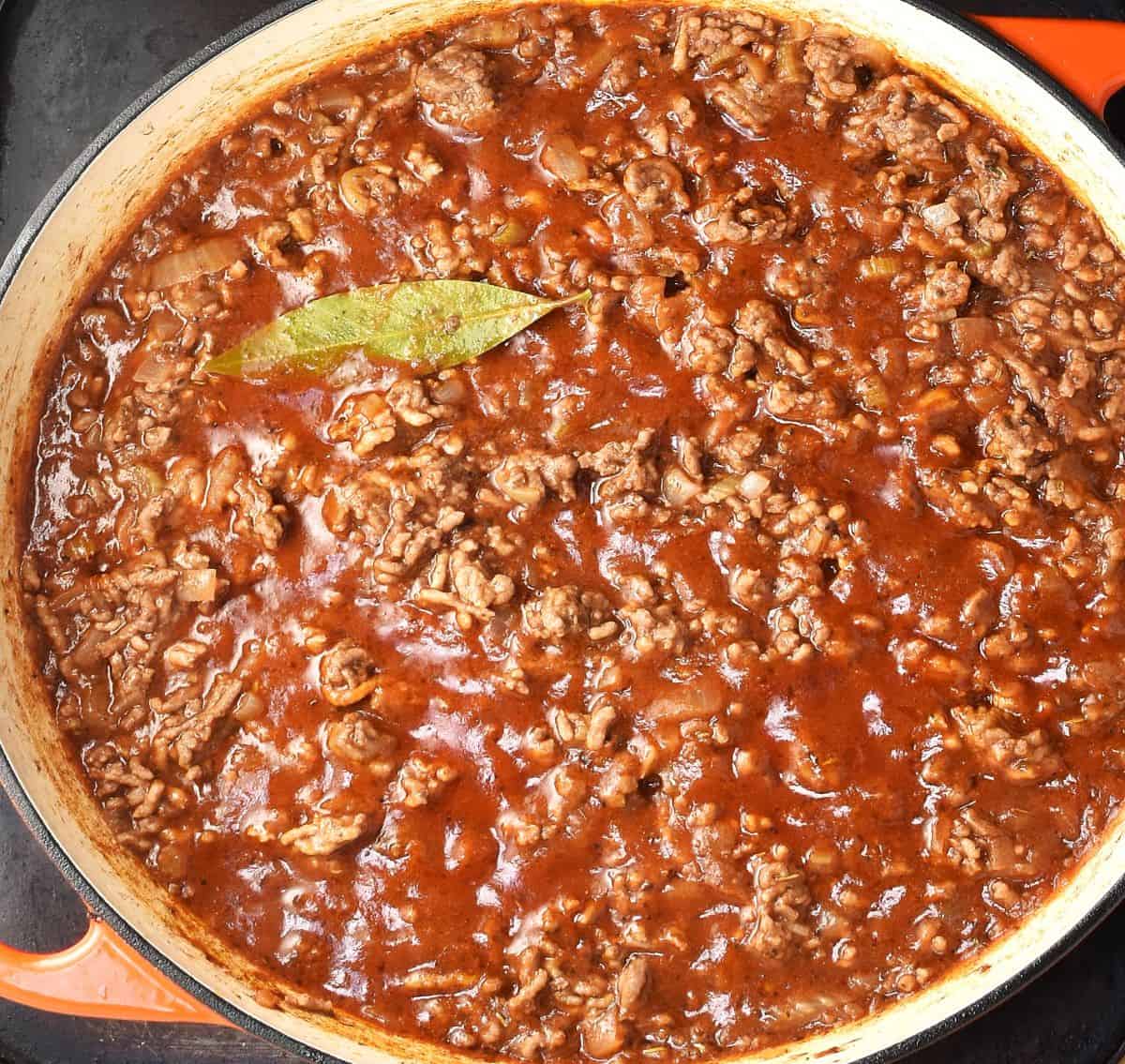 Top down view of rich tomato meat potato lasagna filling mixture in round pan.