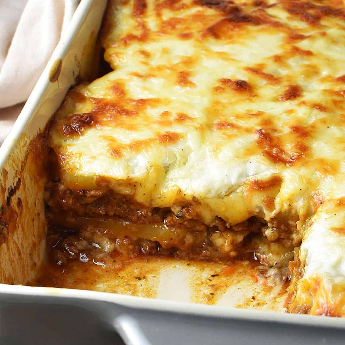 Side view of potato lasagna with meat filling and white sauce in rectangular dish.