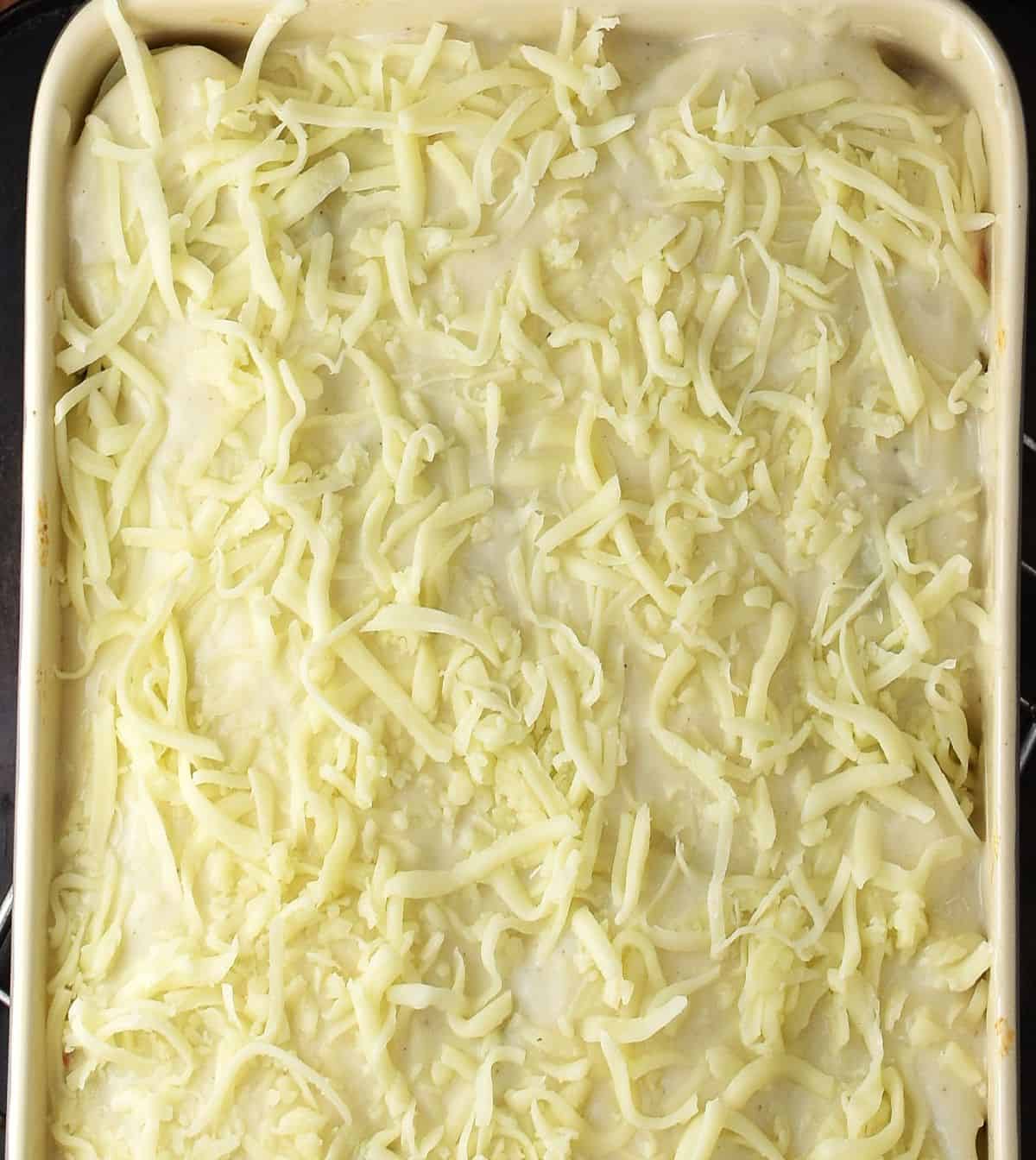 Potato lasagna covered with bechamel sauce and shredded cheese in rectangular dish.