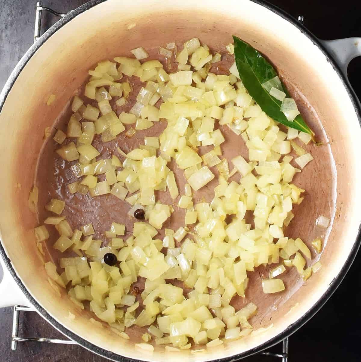 Top down view of chopped onion and bay leaf in pot.