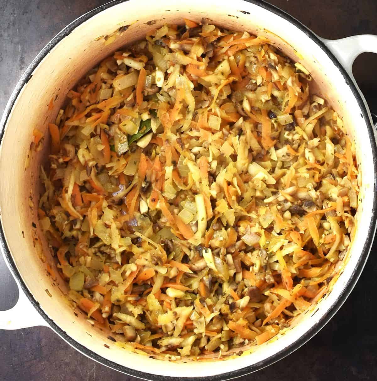 Cooked shredded vegetables with mushrooms for soup in large white pot.