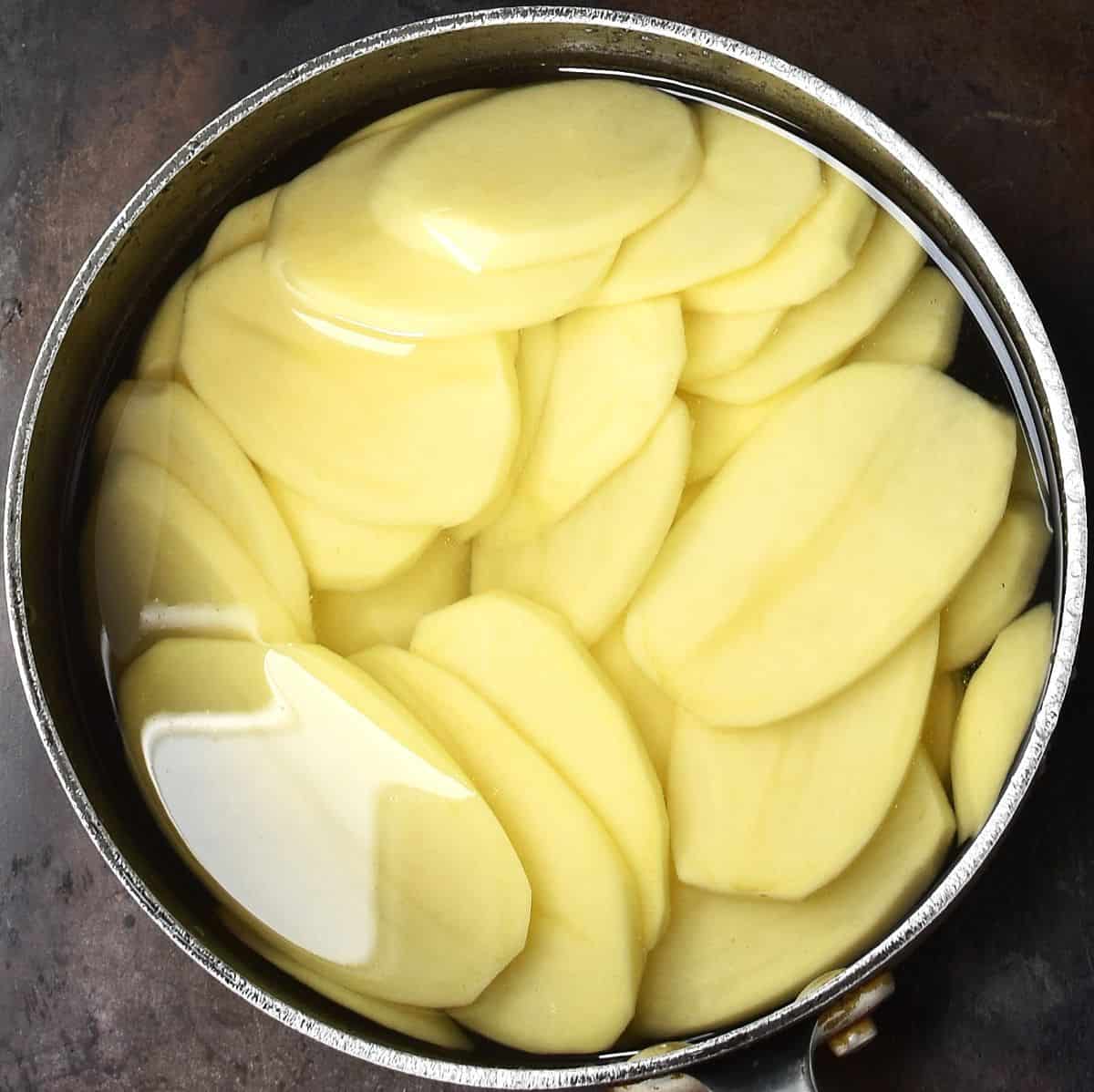 Slices of potato in pot with water.
