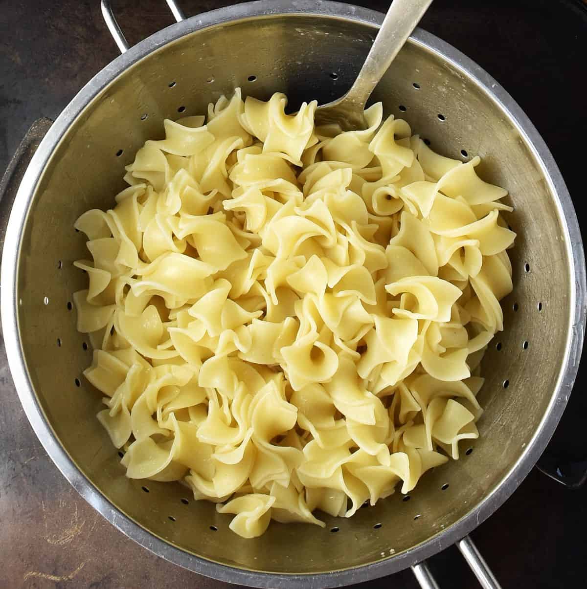 Top down view of cooked pasta with spoon in strainer.