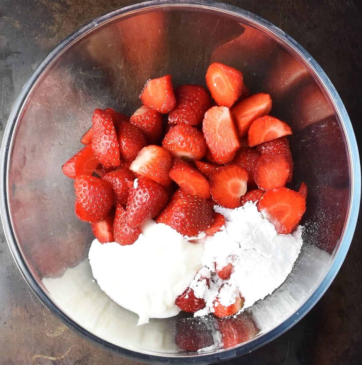 Top down view of chopped strawberries and sour cream in glass bowl.