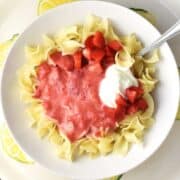 Top down view of strawberry pasta with sour cream and spoon in white bowl.