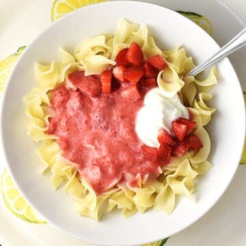 Top down view of strawberry pasta with sour cream and spoon in white bowl.