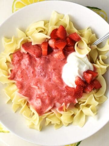 Top down view of strawberry pasta with sour cream and spoon in white bowl.
