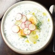 Top down view of creamy Polish cucumber soup with radish, eggs and potatoes in grey bowl.