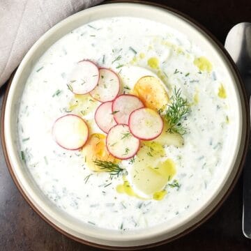 Top down view of creamy Polish cucumber soup with radish, eggs and potatoes in grey bowl.