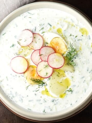 Top down view of creamy Polish cucumber soup with radish, eggs and potatoes in grey bowl.