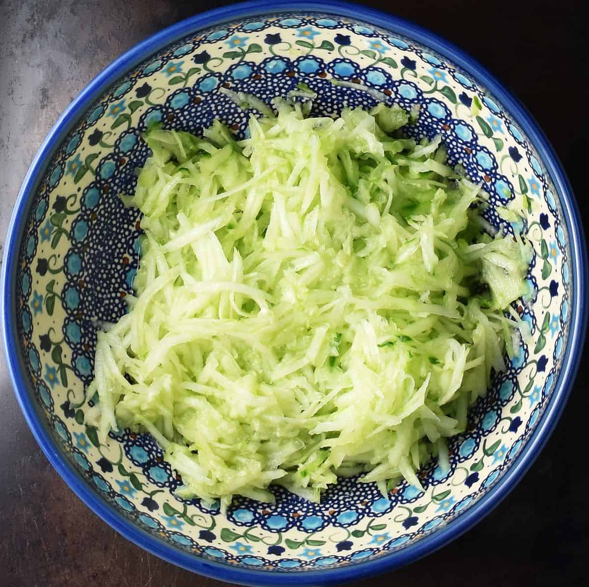 Top down view of grated cucumber in blue ceramic bowl.
