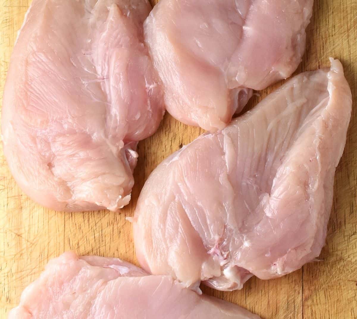 Top down view of 4 chicken breasts on top of cutting board.