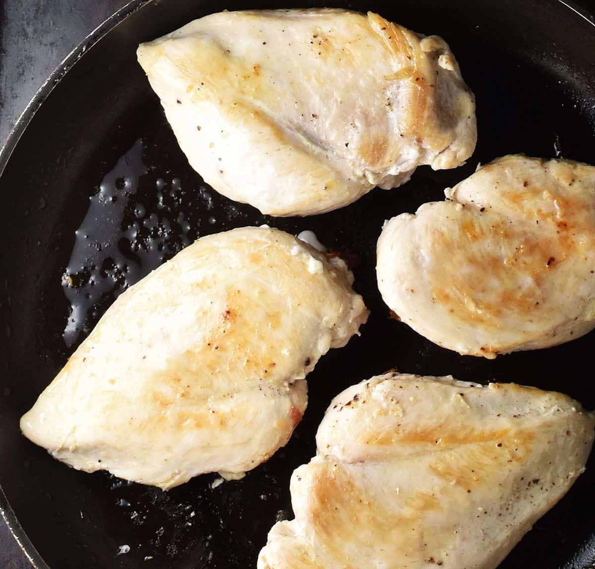 4 seared skinless chicken breasts in frying pan.