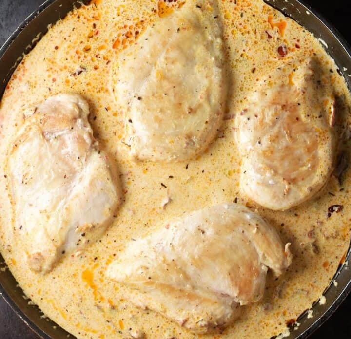 4 seared skinless chicken breast in creamy sauce in skillet.