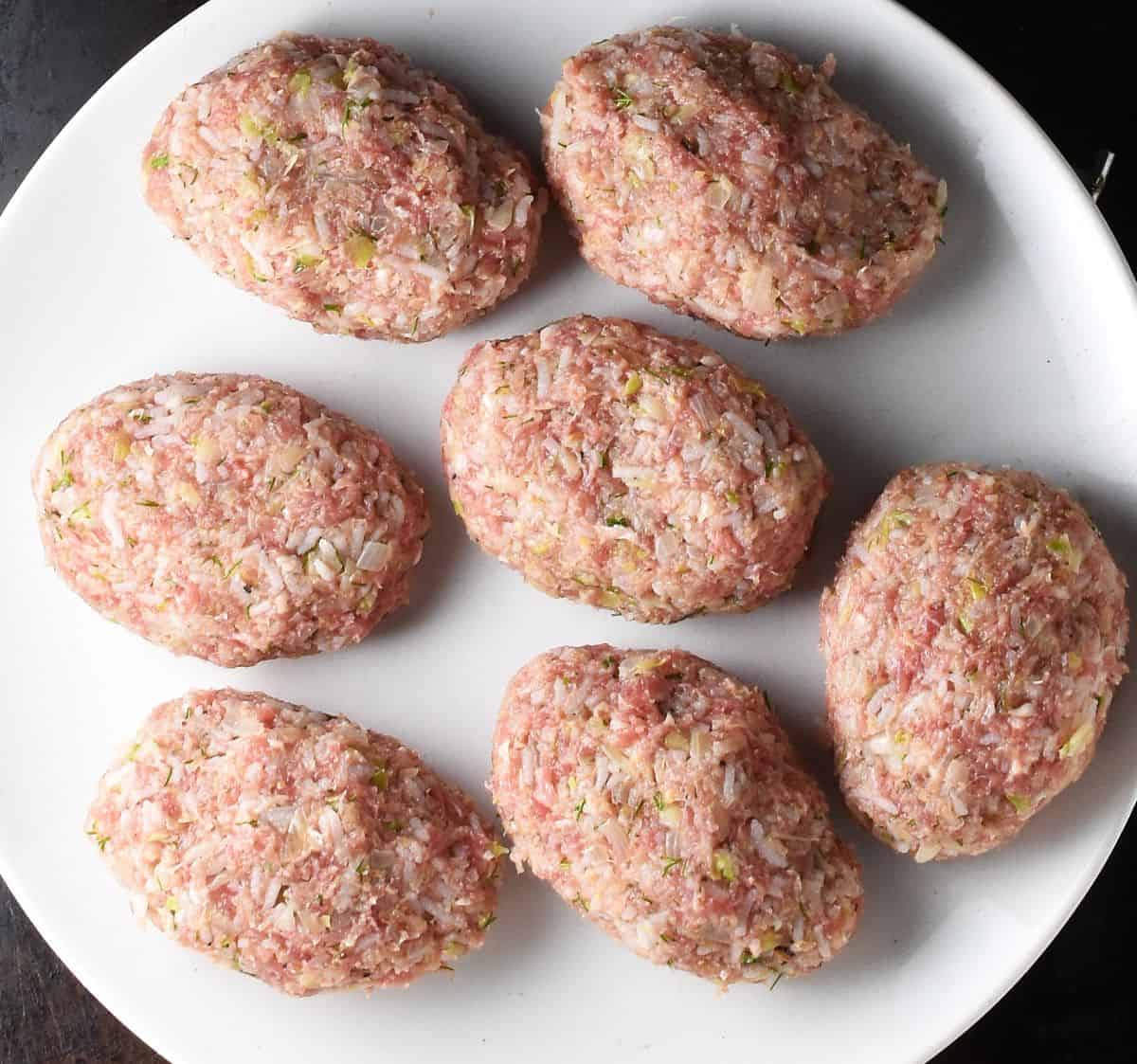 7 uncooked lazy cabbage rolls on white plate.