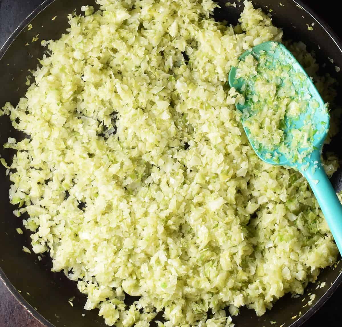 Top down view of sauteed cabbage in large pan with blue spoon.