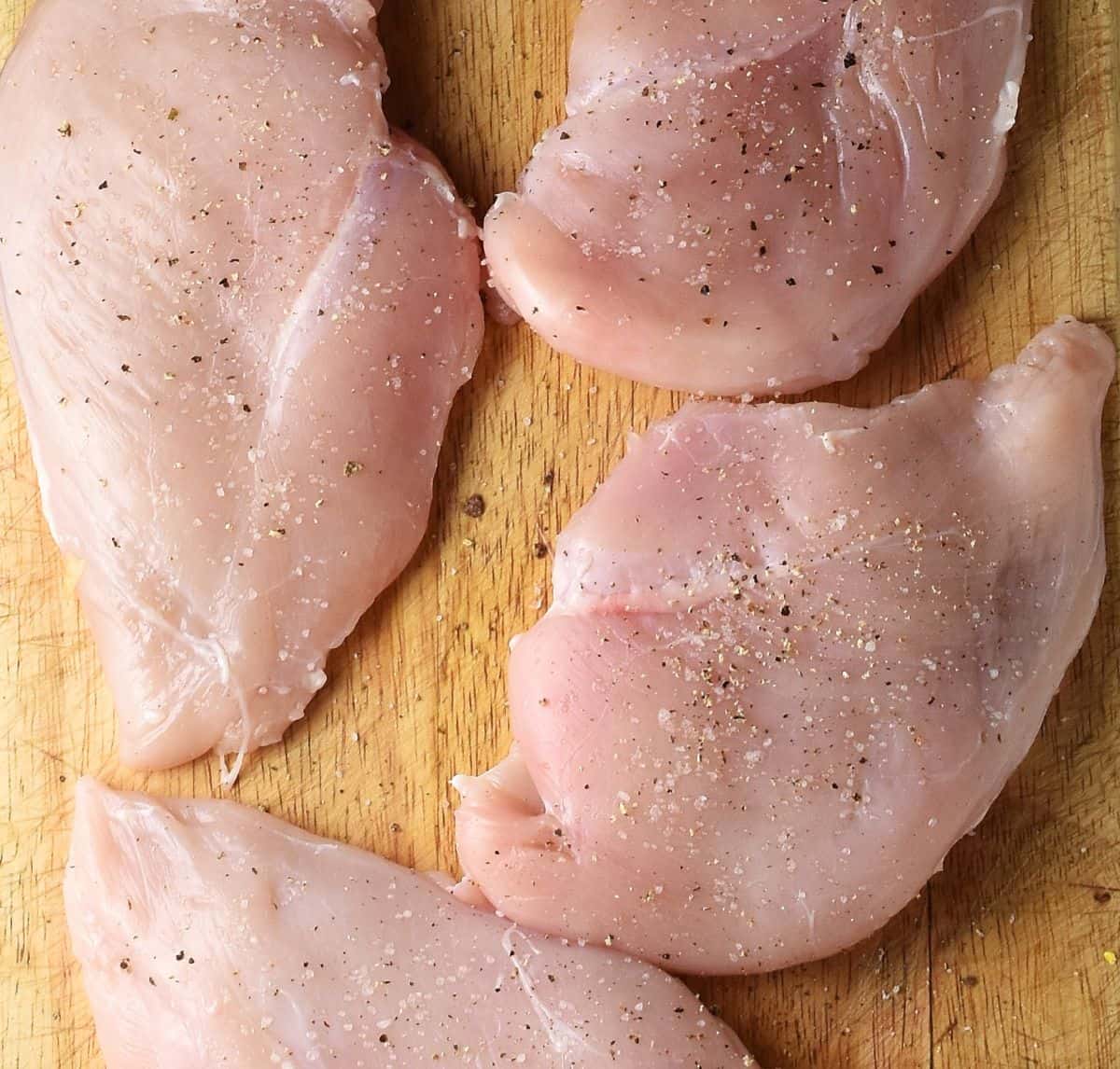 Top down view of 4 skinless chicken breasts on top of wooden board.