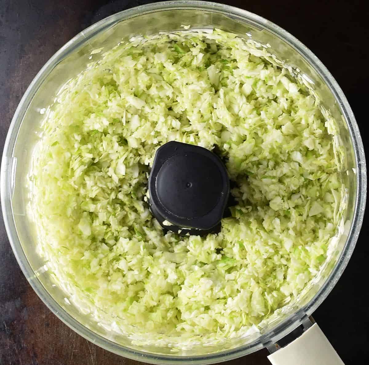 Top down view of finely chopped cabbage in food processor bowl.