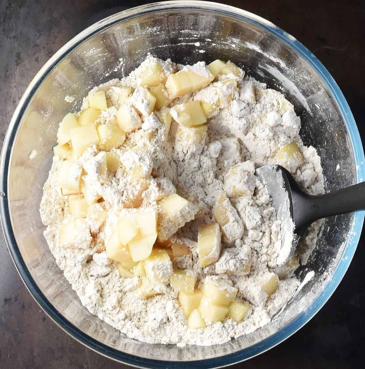 Cubed pear with dry mixture and black spoon in glass bowl.