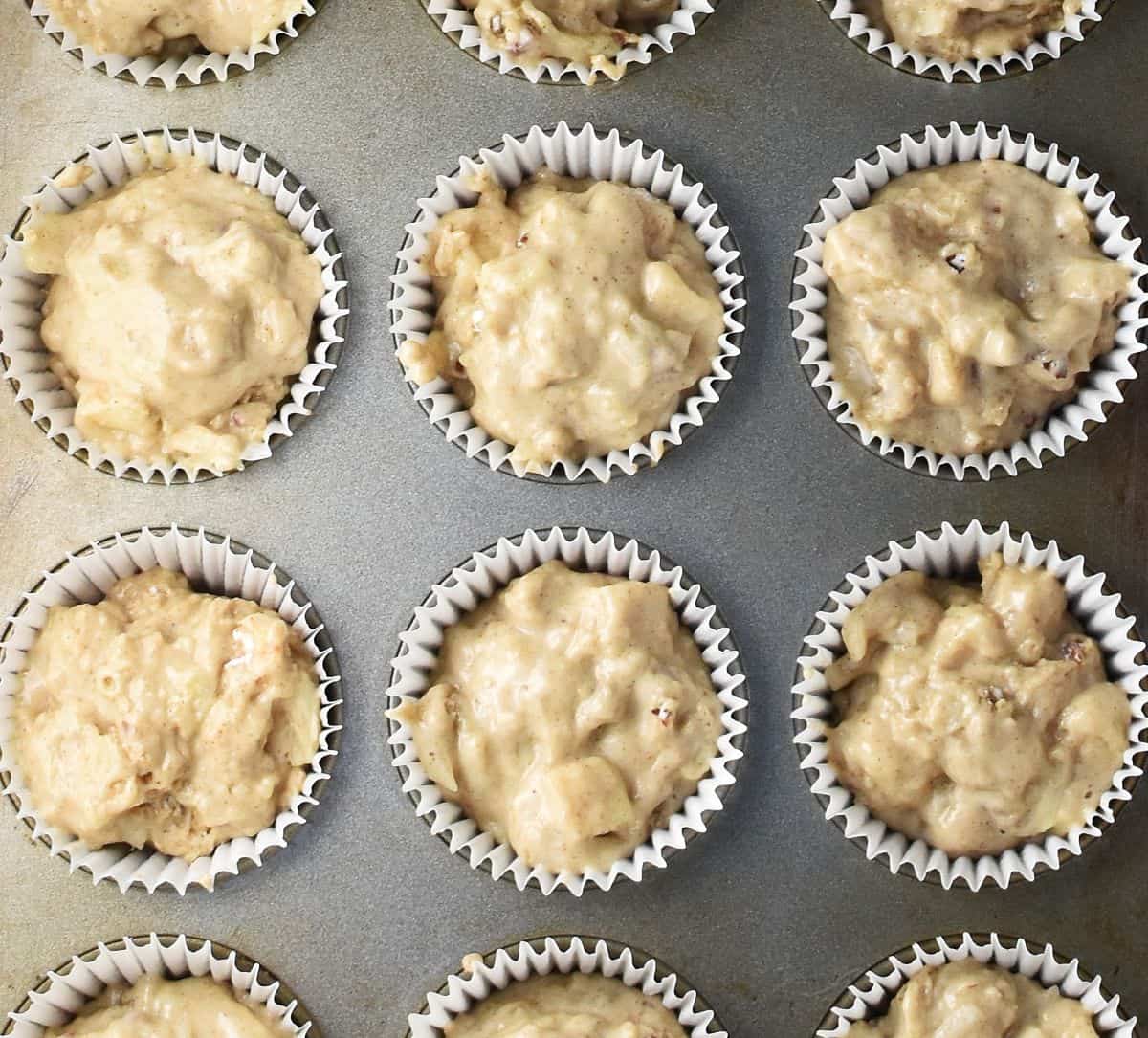 Top down view of muffin batter with pear in white paper cases in pan.