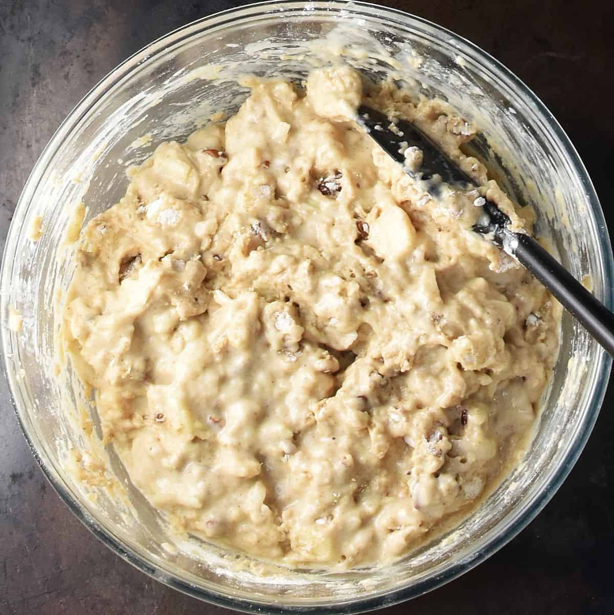 Pear muffin batter with black spoon in large glass bowl.