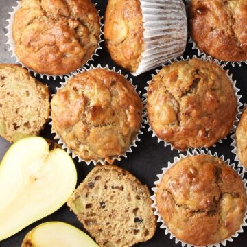 Top down view of pear muffins in white paper cases and halved pear.