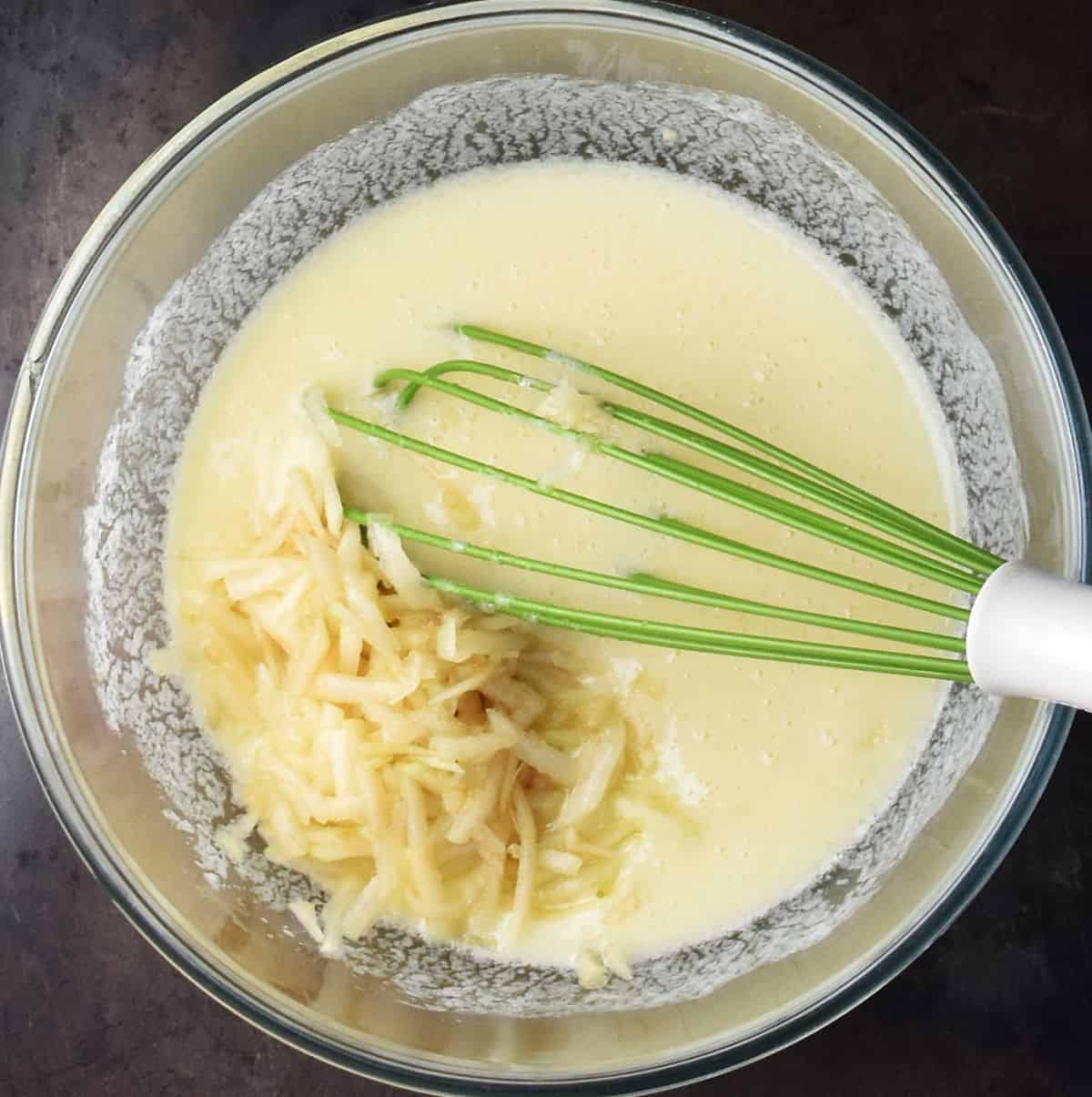 Wet muffin mixture with grated pear and green whisk in glass bowl.