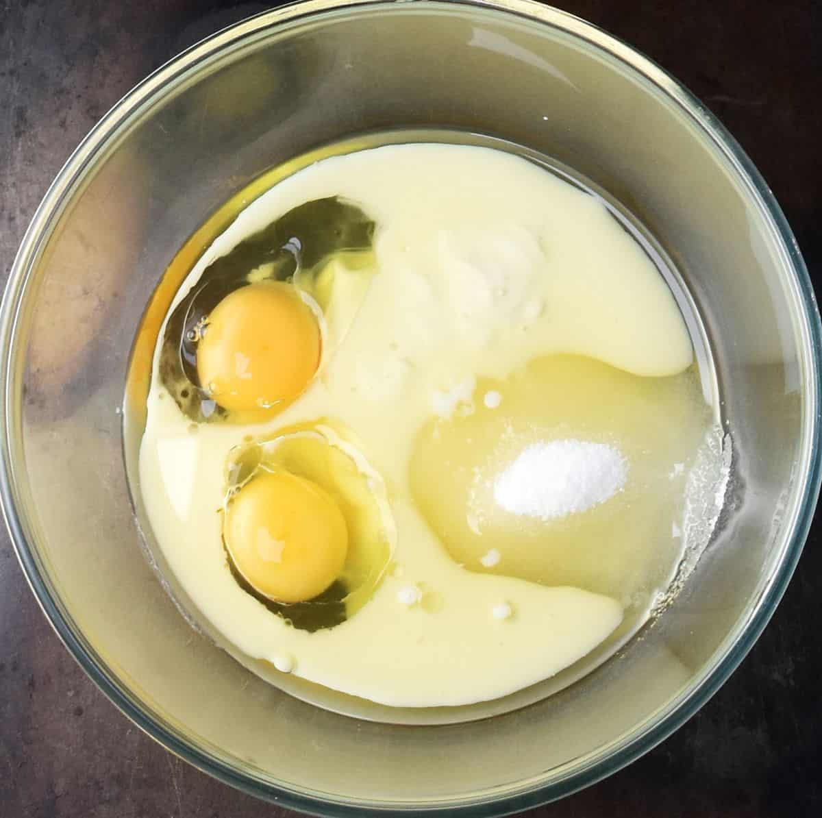 Top down view of 2 eggs, yogurt and oil in glass bowl.