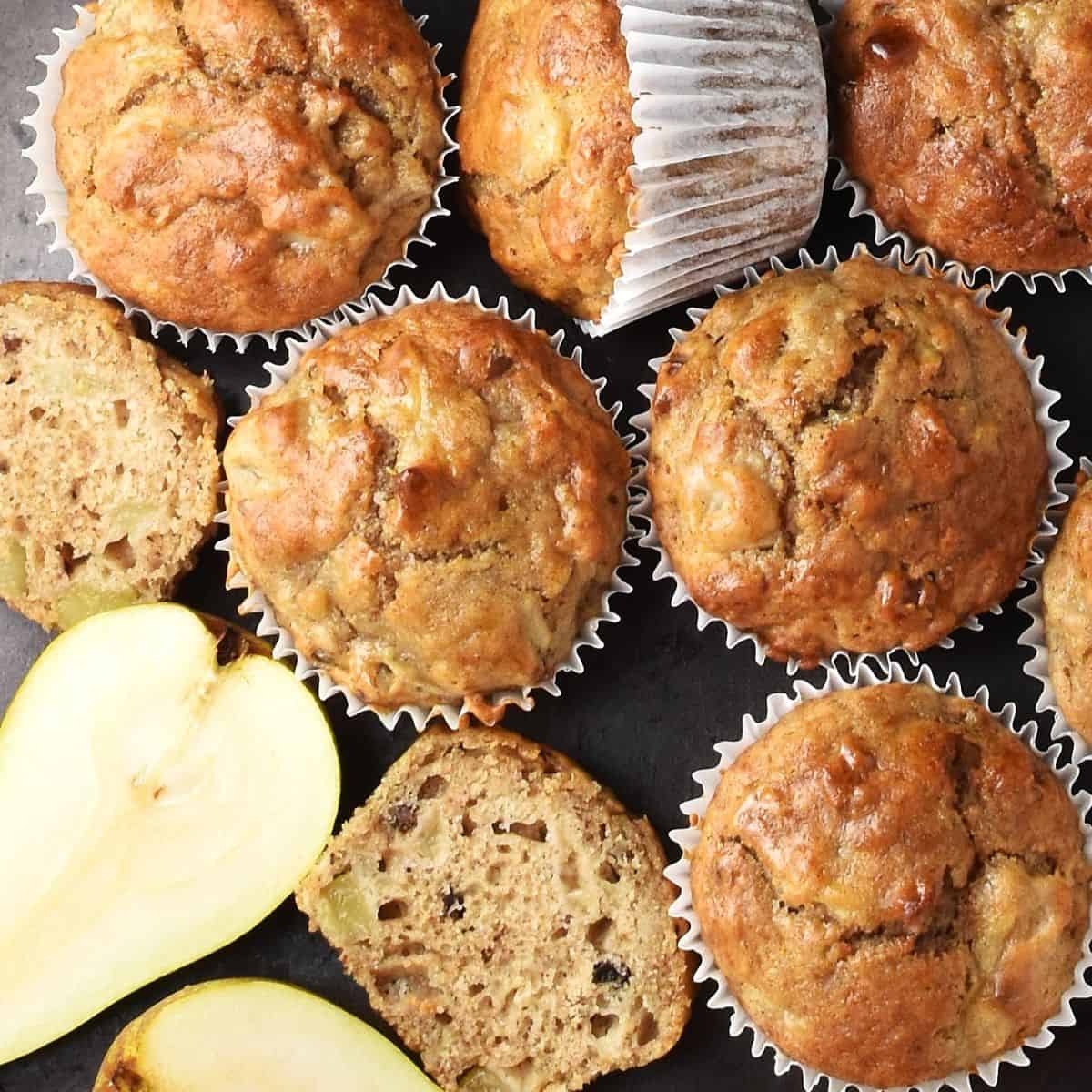 Top down view of pear muffins in white paper cases and halved pear.