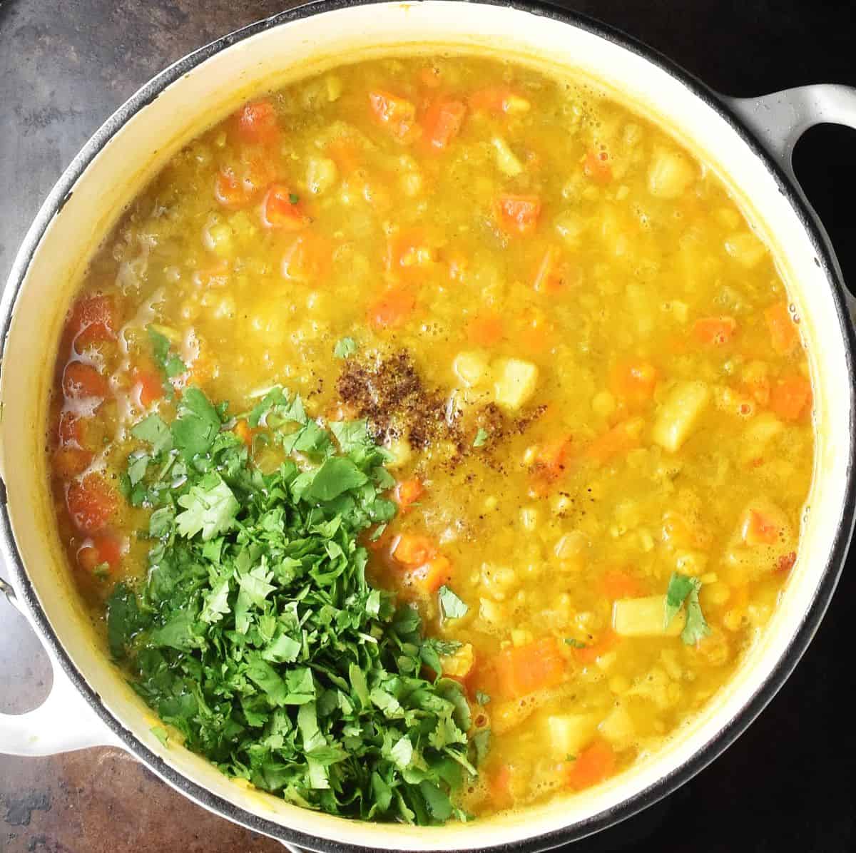Chunky vegetable mulligatawny with fresh chopped cilantro in white pot.