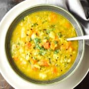 Close-up top down view of vegetable mulligatawny soup in green bowl with spoon on white plate.