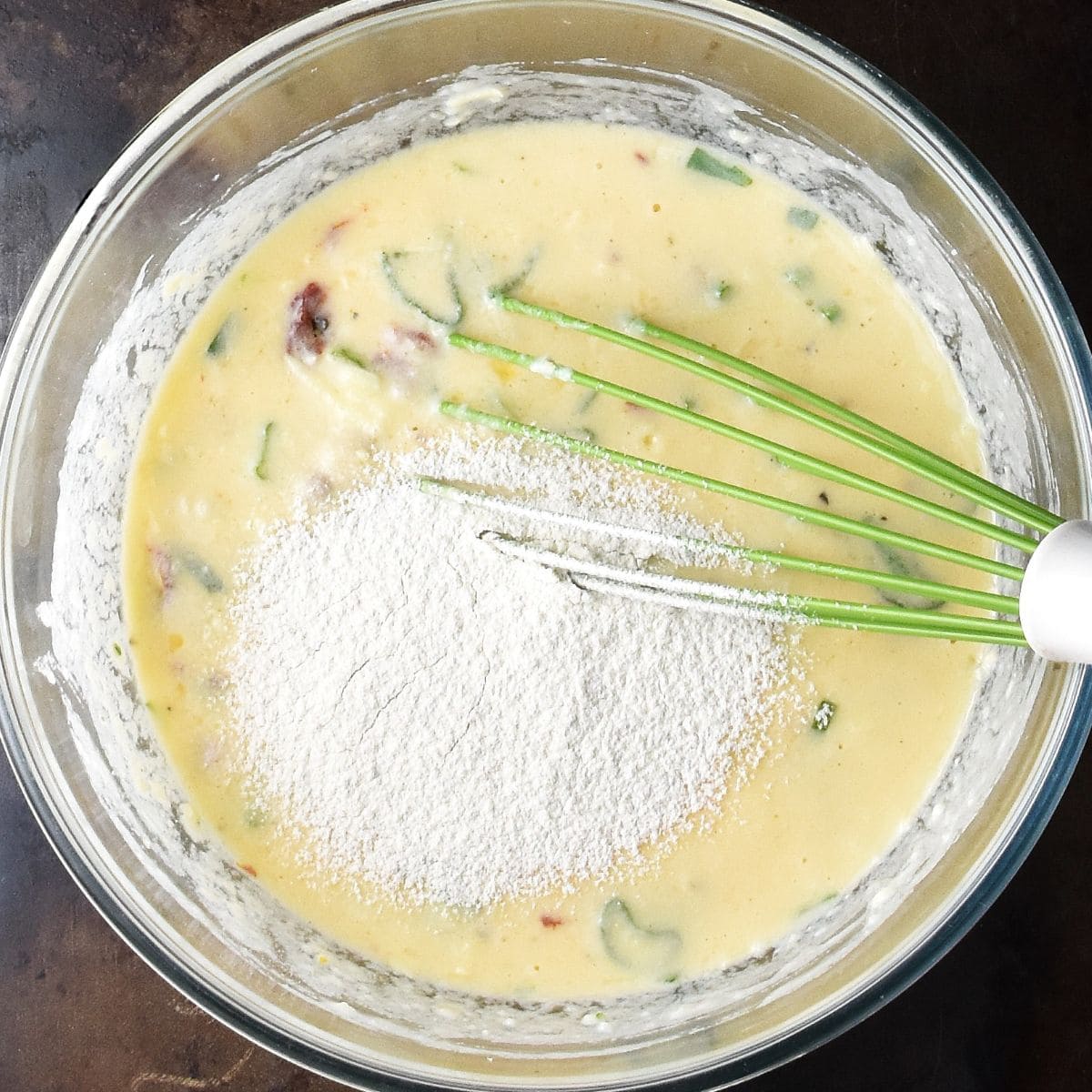 Top down view of egg potato muffin batter with flour in glass bowl with whisk.