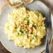 Top down view of creamy scrambled eggs with chives on spotted grey plate with fork.