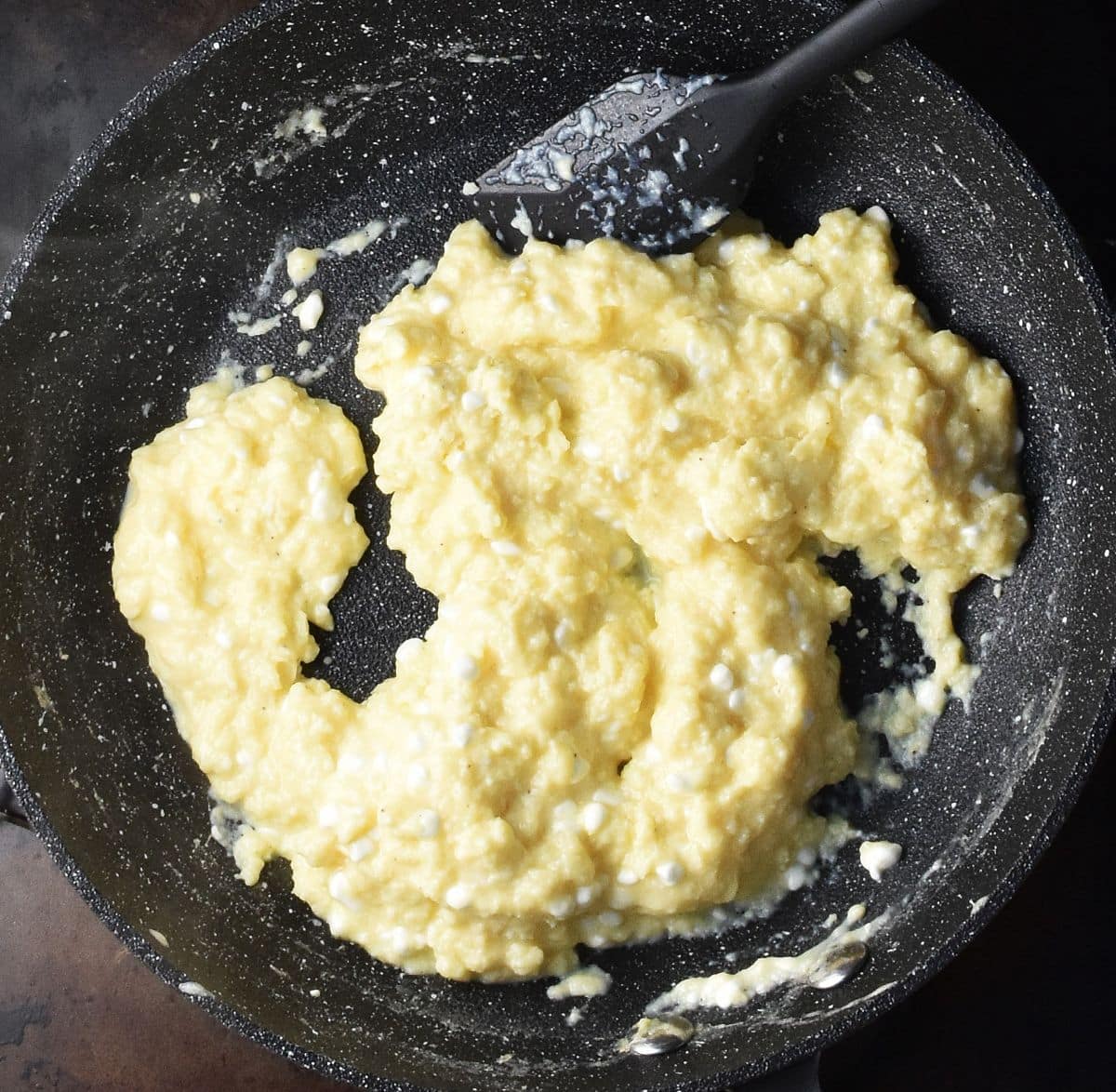 Top down view of creamy cottage cheese scrambled eggs in black pan with black spatula.