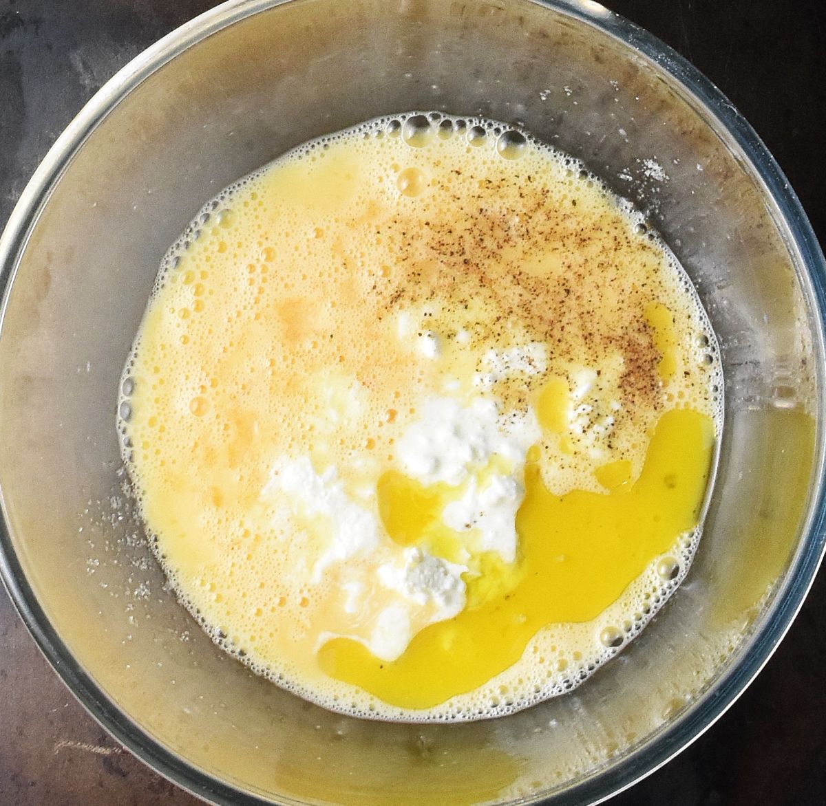 Cottage cheese and seasoning with creamy egg mixture in glass bowl.