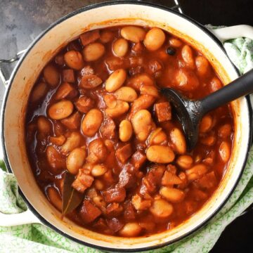 Top down view of Polish beans in tomato sauce in white pot with black spoon.