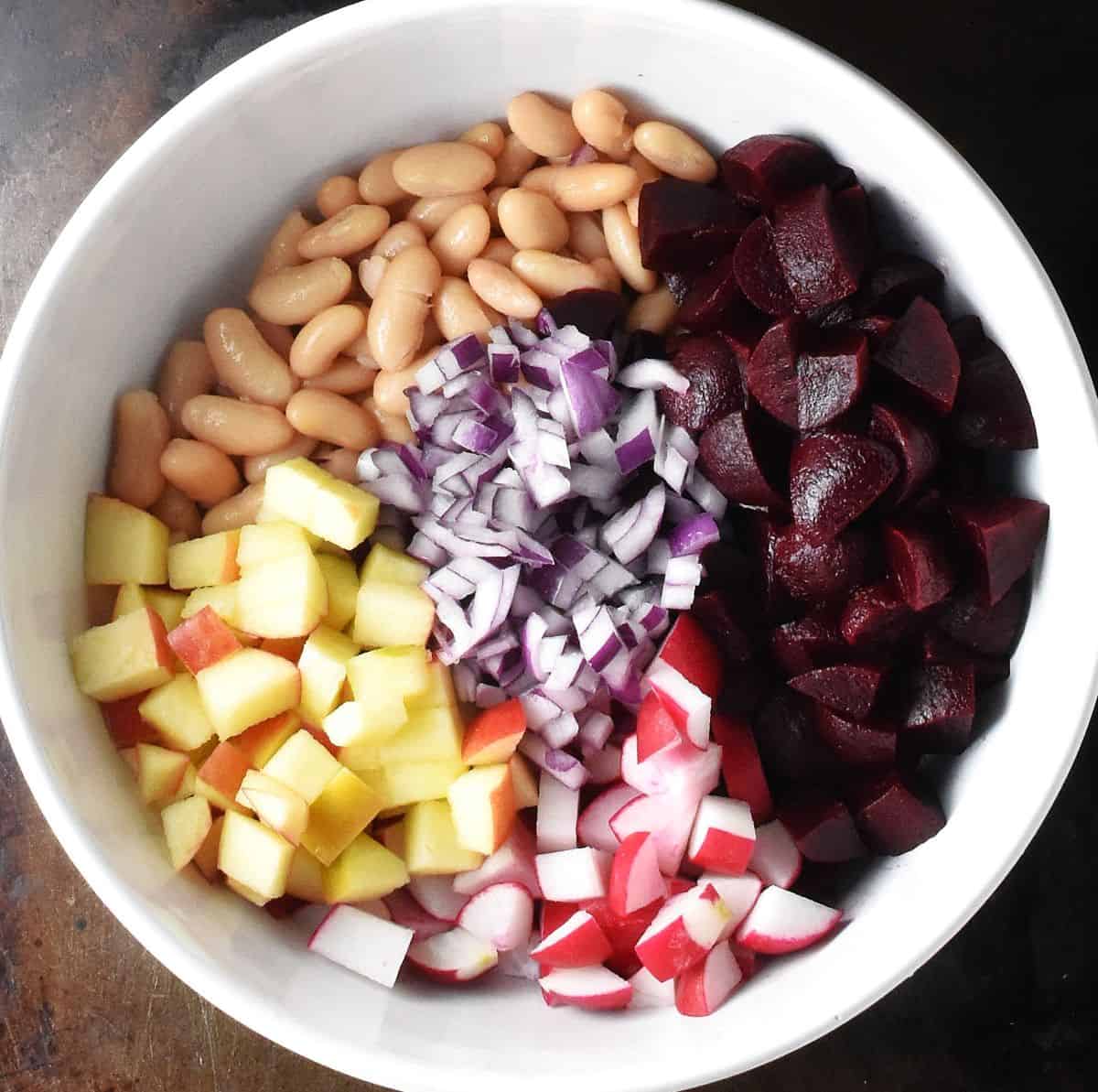 Top down view of cubed pickled beets, apple, beans and chopped red onion in white bowl.