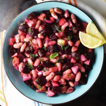 Top down view of pickled beet salad in blue bowl with lemon wedges.