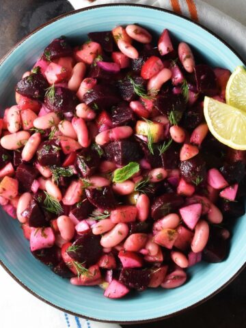 Top down view of pickled beet salad in blue bowl with lemon wedges.