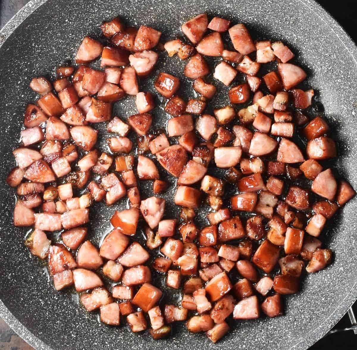 Top down view of cubed fried kielbasa sausage in large pan.