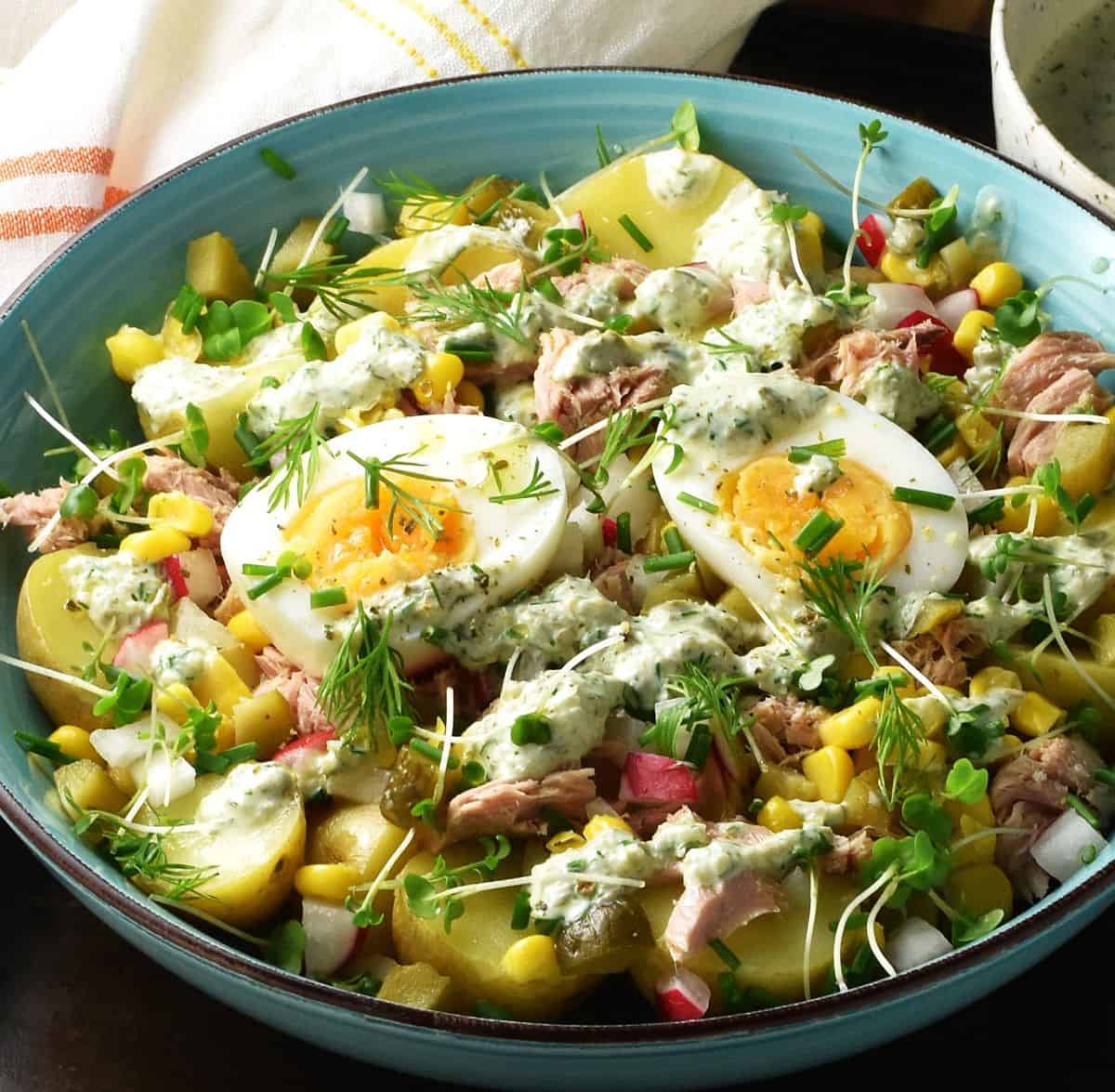 Side view of tuna, potato and egg salad with herbs in blue bowl.