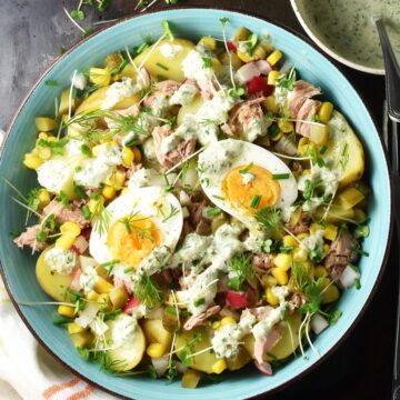 Top down view of potato tuna salad with eggs, herbs and creamy dressing in blue bowl.