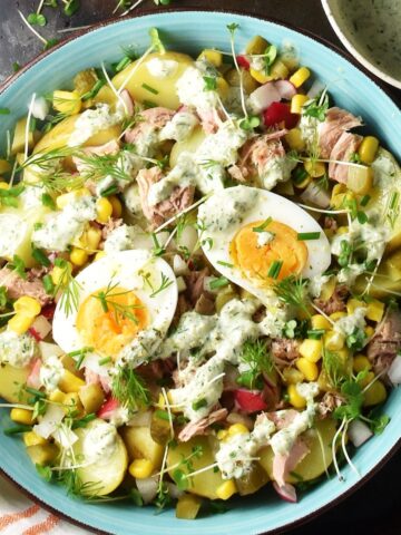 Top down view of potato tuna salad with eggs, herbs and creamy dressing in blue bowl.
