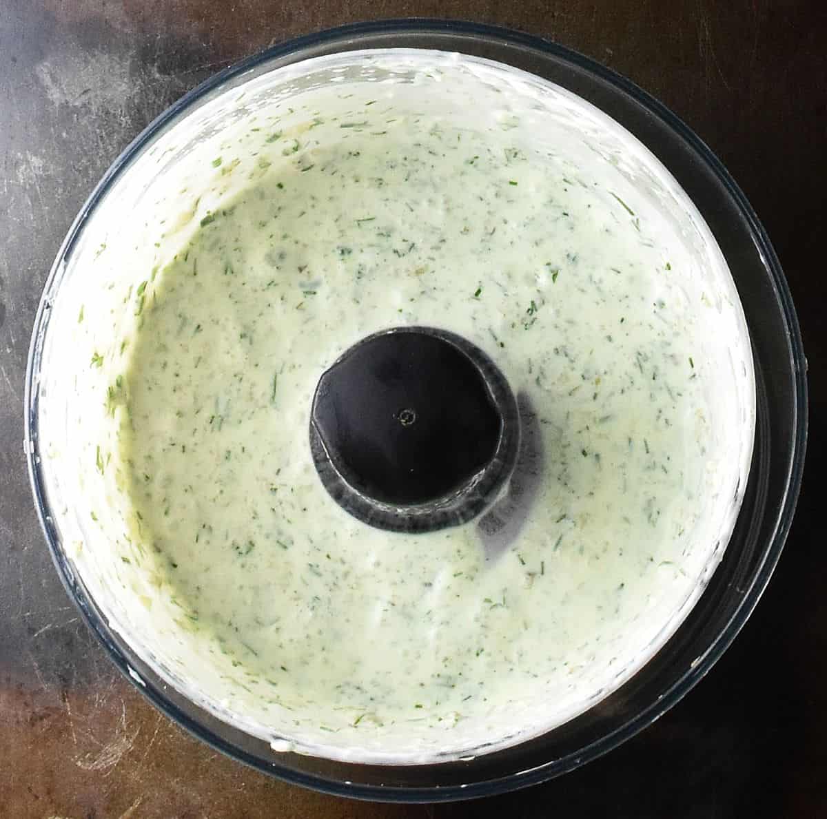 Top down view of creamy dressing sauce in food processor bowl.