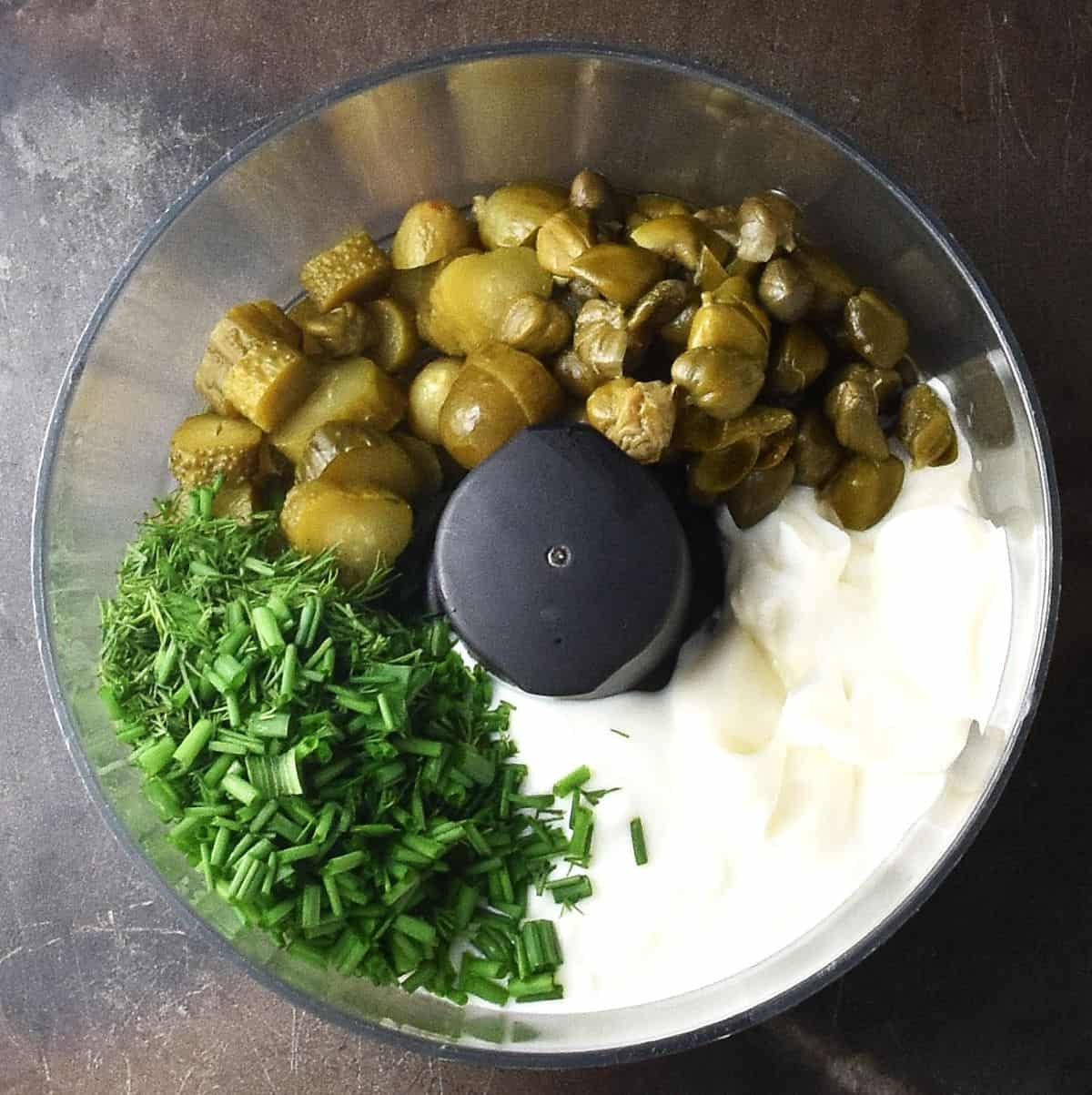 Yogurt, chopped dill pickles, capers and herbs in food processor bowl.